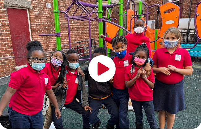 A group of students, all wearing masks, standing outside on the playground.