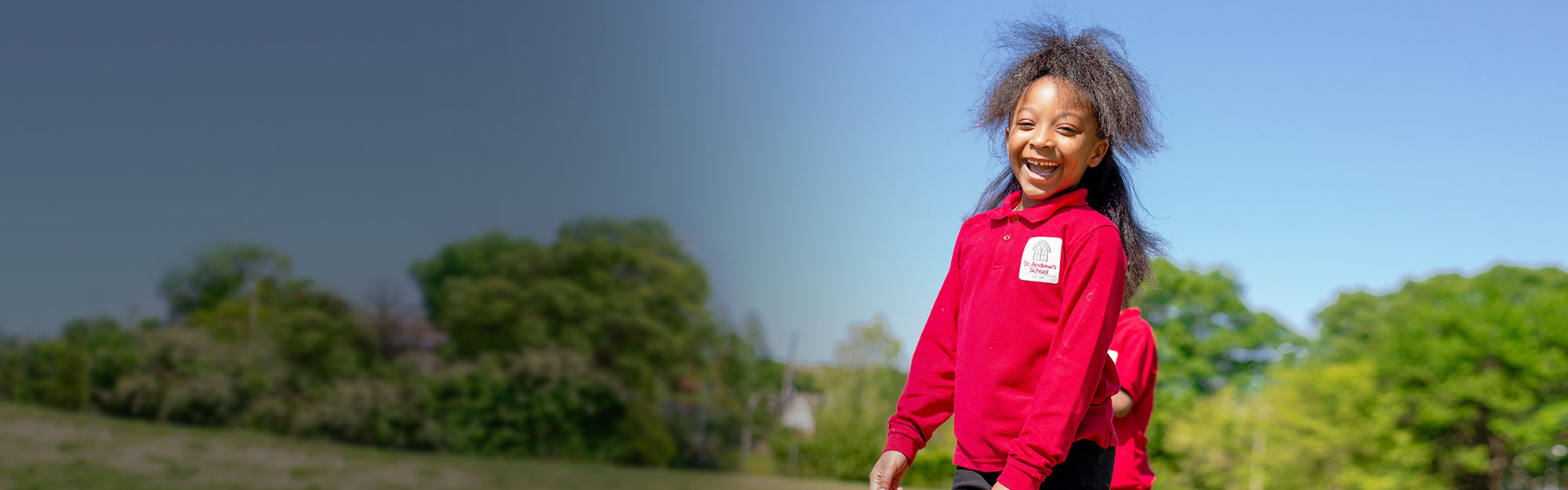 A smiling St. Andrew's School student against a blue sky.