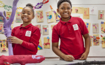 Two students smile in a classroom while working on a project.