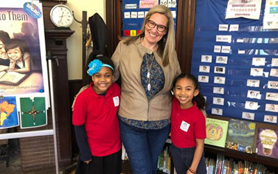 Volunteer Natalie Foster stands with two students.