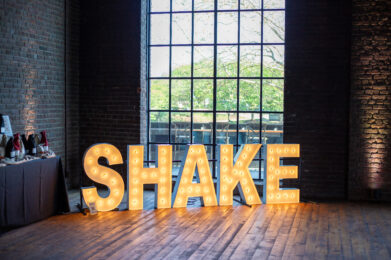 Neon lights reading "SHAKE" on the floor in front of a window.