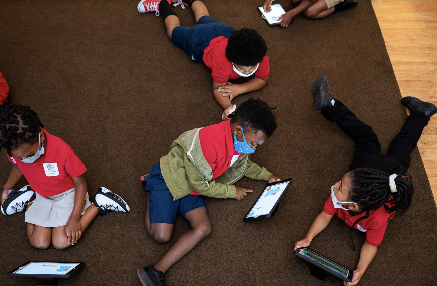 Kindergarten students who are spread out on the carpet, completing activities on their tablets.