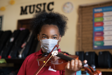 A student wearing a face mask and playing the violin.