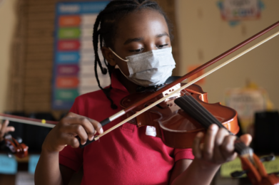 A student wearing a face mask and playing the violin.