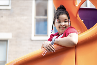 A student smiles at the camera while seated on a slide.